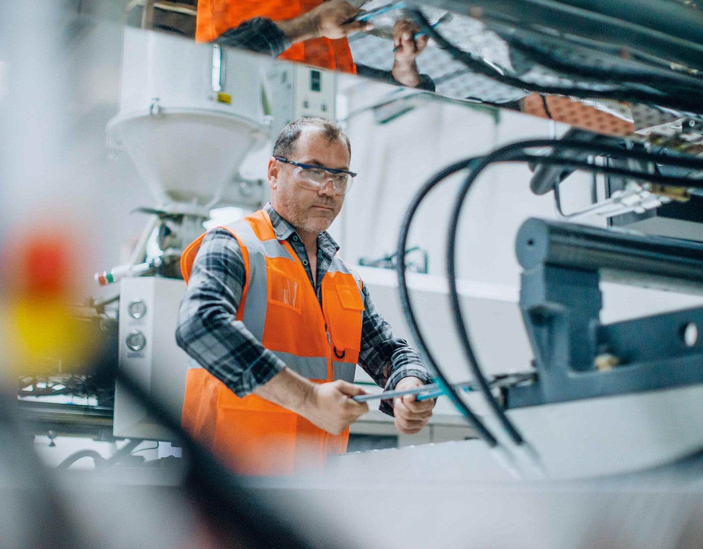 A man in an orange vest and safety goggles operates a machine.